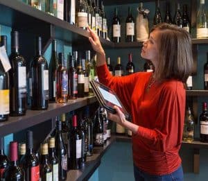 a person holding a tablet in front of a shelf of wine bottles 