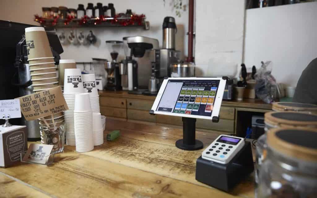 a tablet on a counter with a cash register and coffee cups